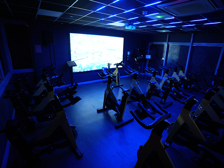 A line of spinning bikes in a dark room, a large screen at the front
