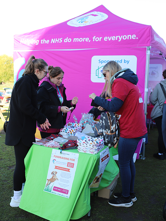 A pink tent next to a table with a green table cloth, one person behind the table and two people stood at the opposite side of the table