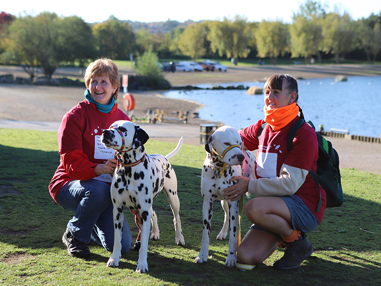 Two females bending down on grass each holding on to a Dalmation