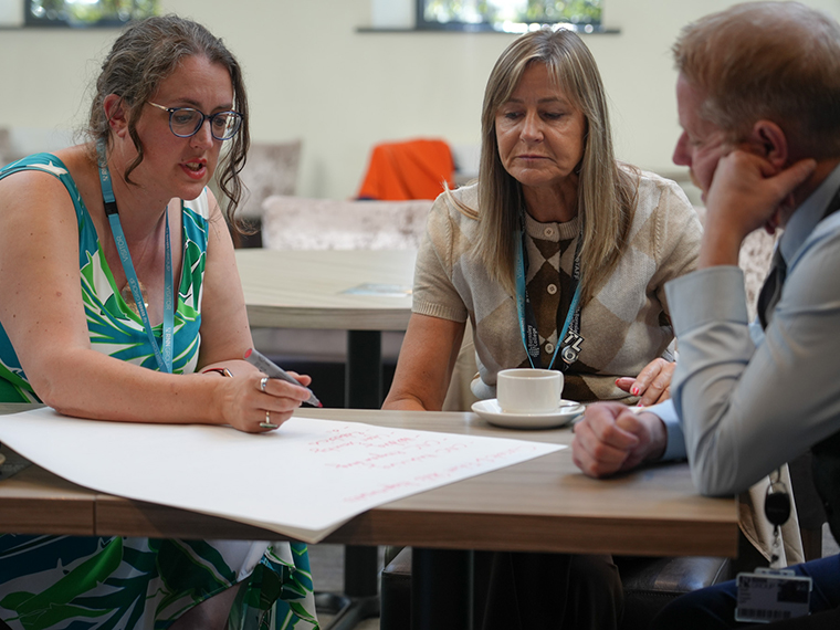 Three people sat around a table one person writing on a large sheet of white paper