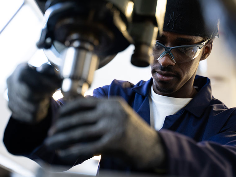 A student in engineering wear using a drill