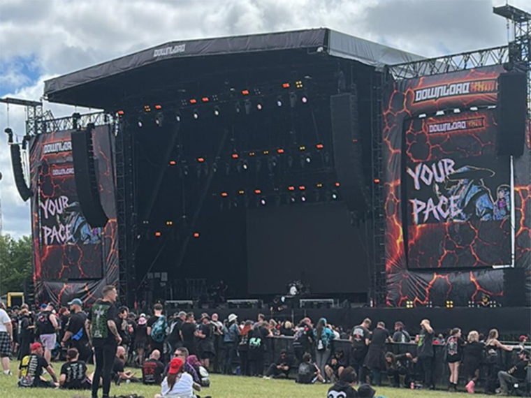 A large black stage in the open air with people stood looking towards it