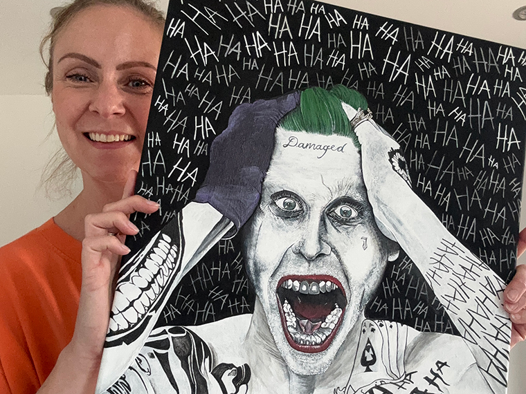 A female in an orange top holding upa painting of a bright white person with their mouth wide open