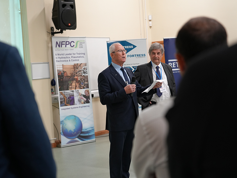 Two males stood in front of an audience, an NFPC pull up banner behind them
