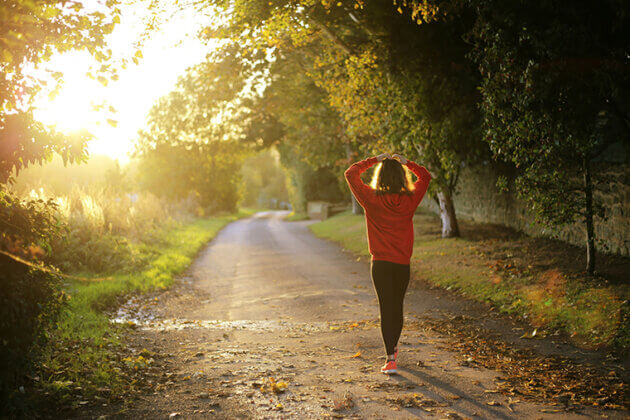 A female walking down a country path with trees either side and the sun shining