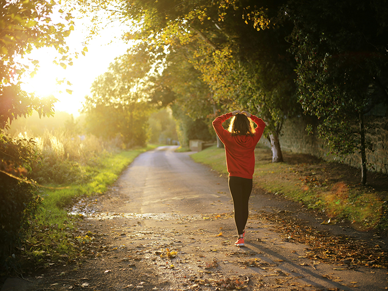 A female walking down a country path with trees either side and the sun shining